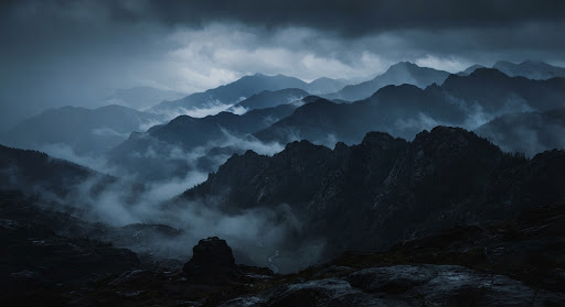 Moody landscape photography, misty mountains layered in deep blues and charcoal tones, minimalistic nature shot.